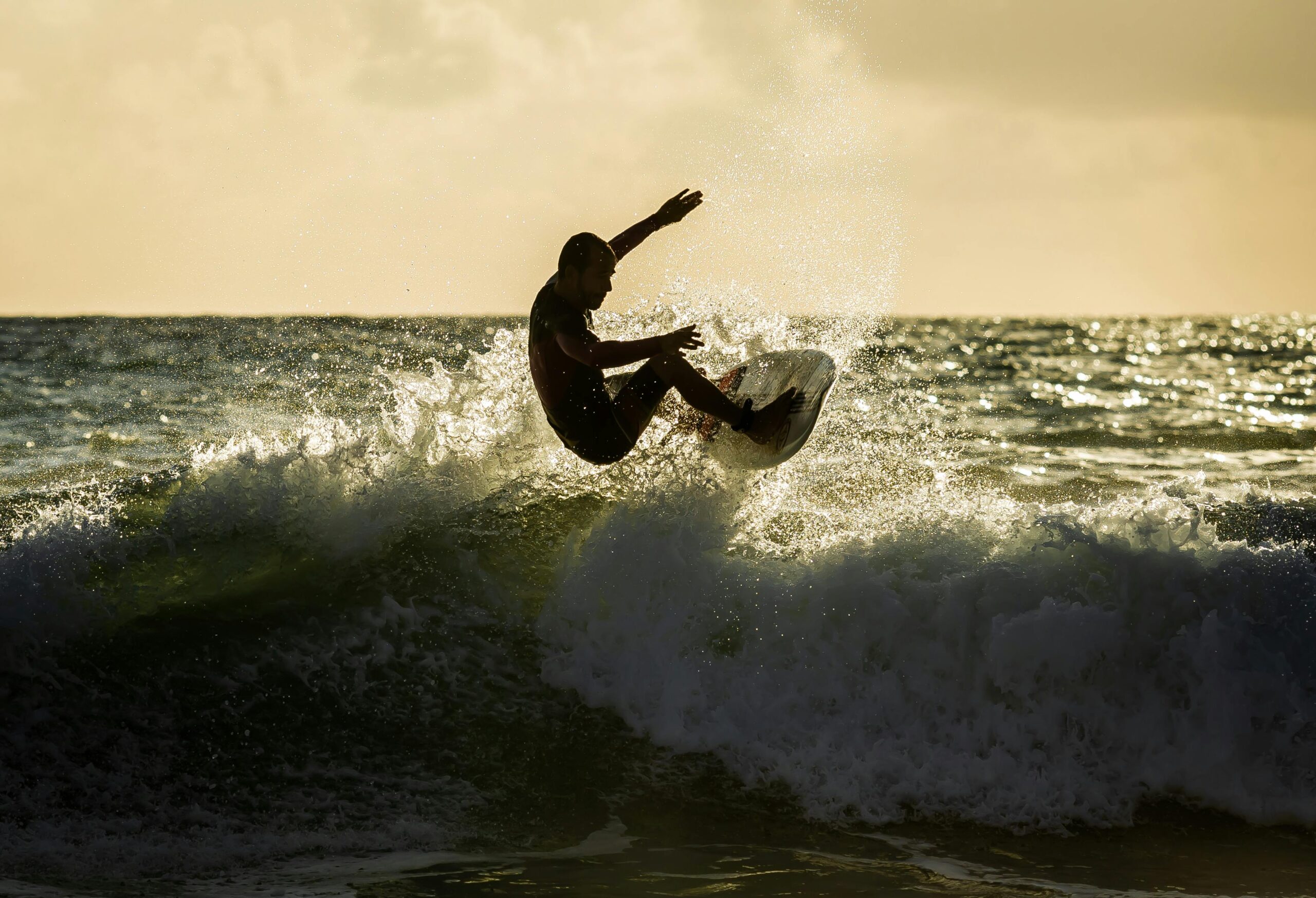 Young man surfing the waves of Zuma Beach while the sun in setting